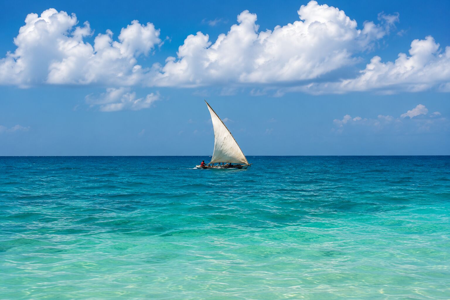 White-sailed ngalawa crossing turquoise water near Kenya's southern coast