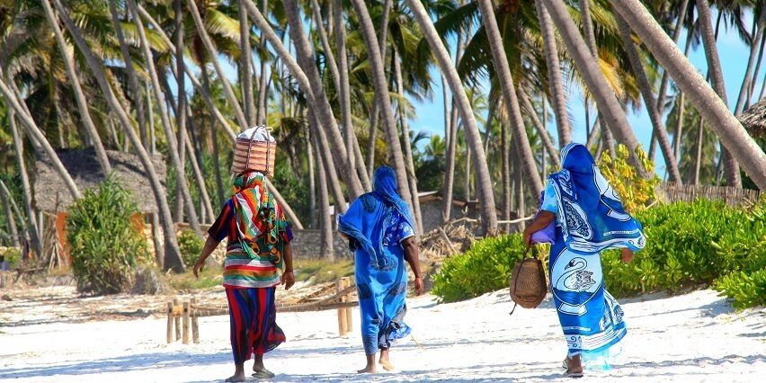 Three residents walking along a palm-lined beach on Kenya's Swahili Coast